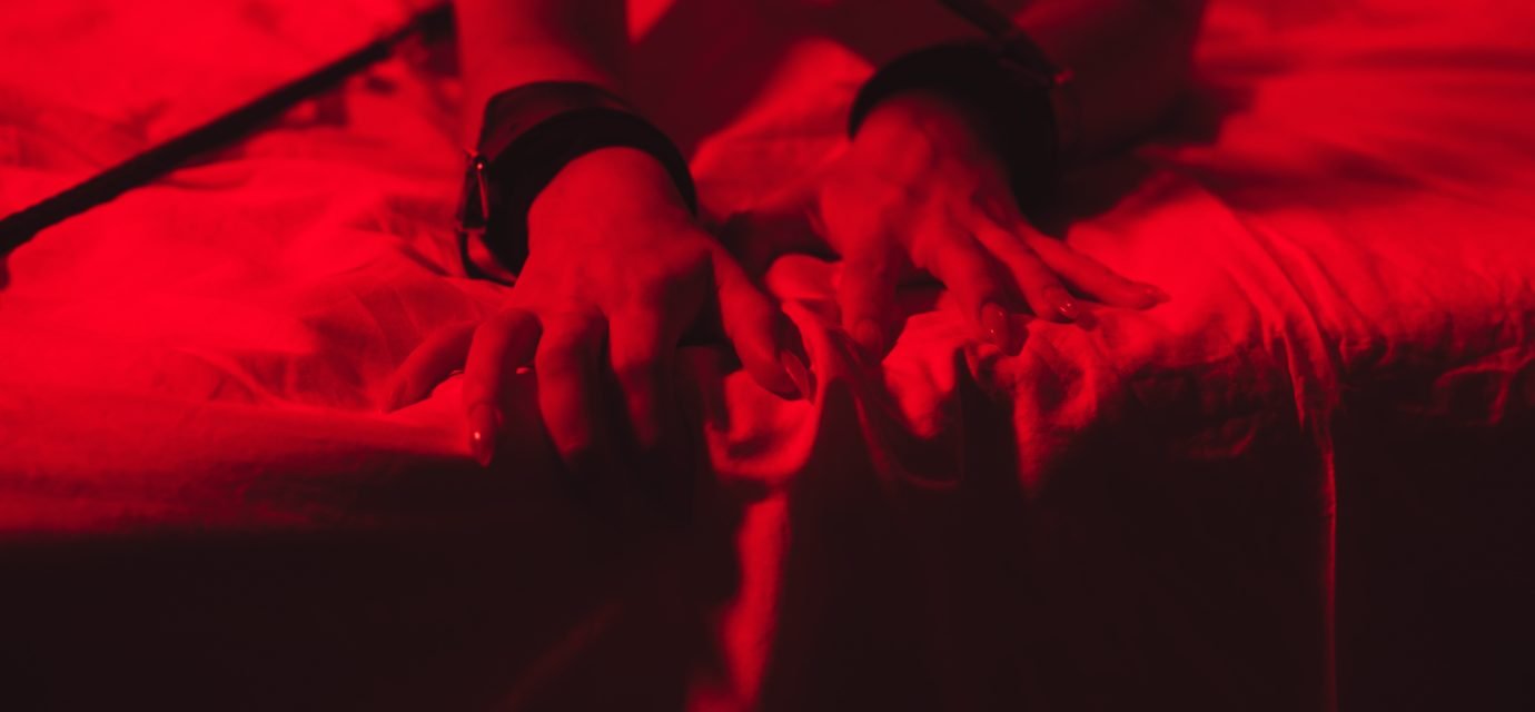 Swingers Club - girl hands in handcuffs and leather whip flogger for BDSM sex with submission and domination lie on bed