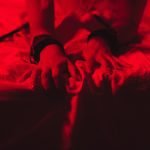 Swingers Club - girl hands in handcuffs and leather whip flogger for BDSM sex with submission and domination lie on bed