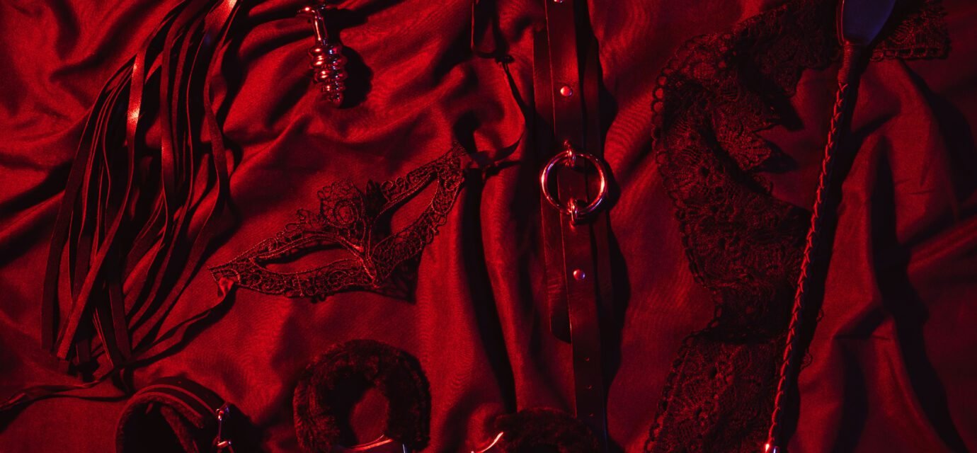 Erotic sex toys for adults for BDSM sex with submission and domination. Handcuffs, mask and leather flogger whip on a black background