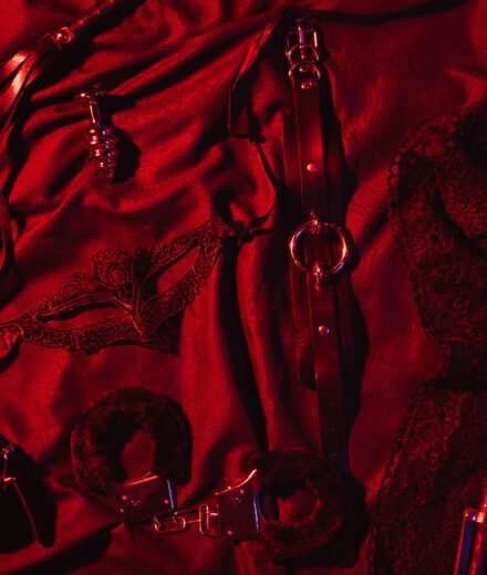 Erotic sex toys for adults for BDSM sex with submission and domination. Handcuffs, mask and leather flogger whip on a black background