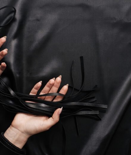 female hands in handcuffs on a dark silk sheet with a whip