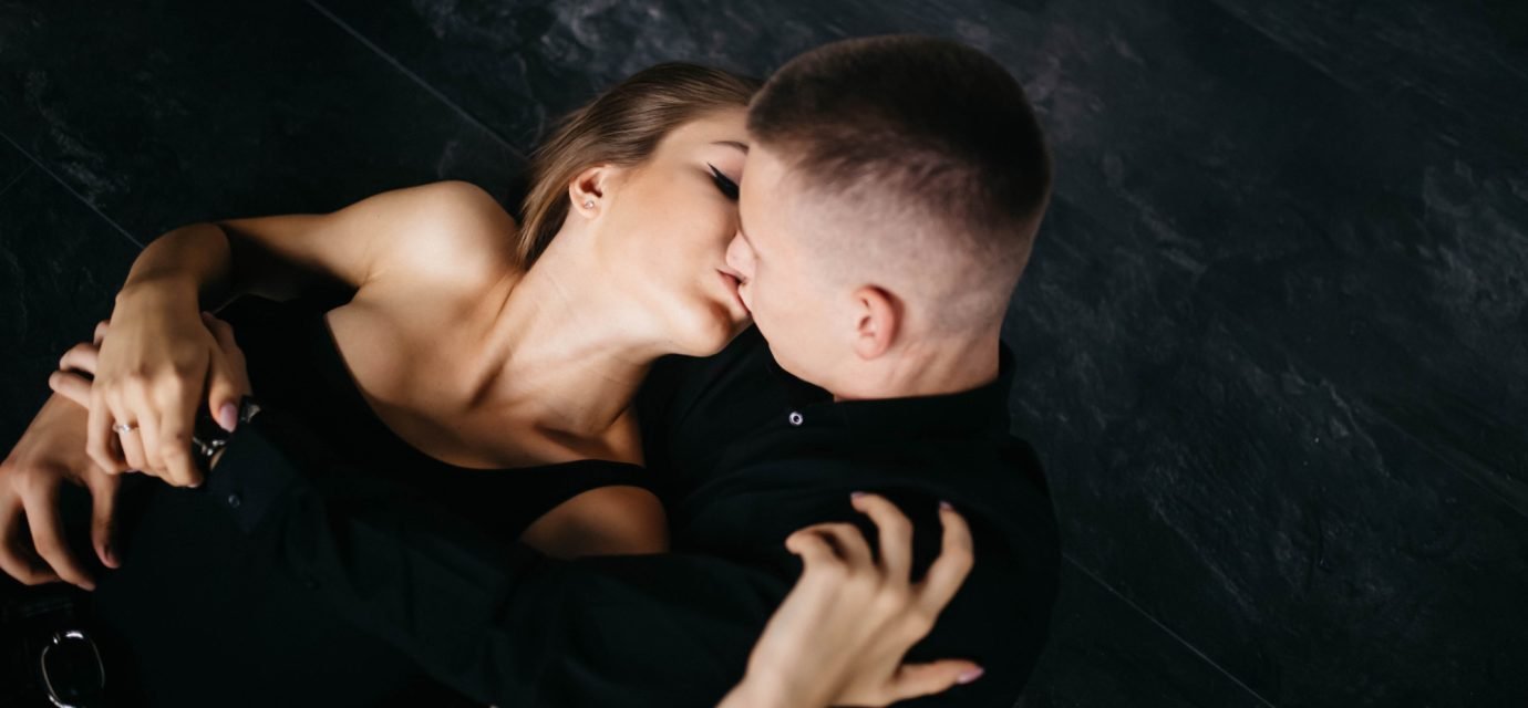 Swingers Club - Man and woman kissing in bed. The guy and the girl sit on the fl