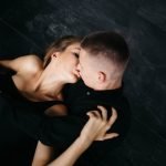 Swingers Club - Man and woman kissing in bed. The guy and the girl sit on the fl