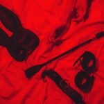 set of BDSM accessories with female hands is lying on the bed. Flogger whip, handcuffs, mask and choker for sex