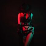 Sexy girl in beautiful underwear, leather belt and hat poses beautifully with neon colored light