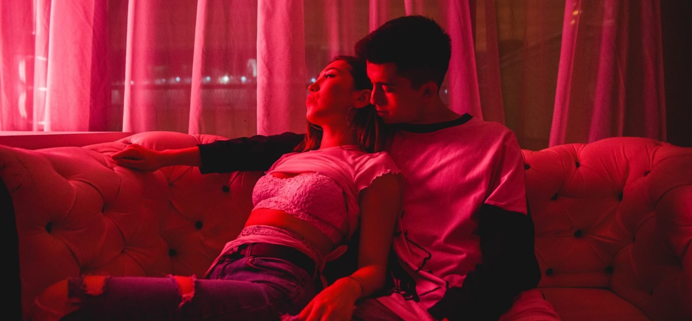 Swingers Club - view-couple-embracing-while-sitting-sofa-illuminated-room